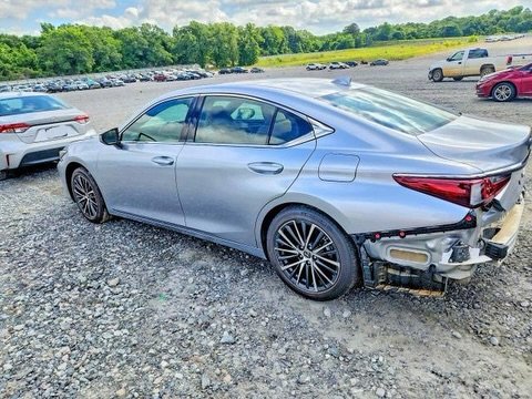 Silver car that has been severely damaged in an accident. The car is parked in a gravel lot with other cars in the