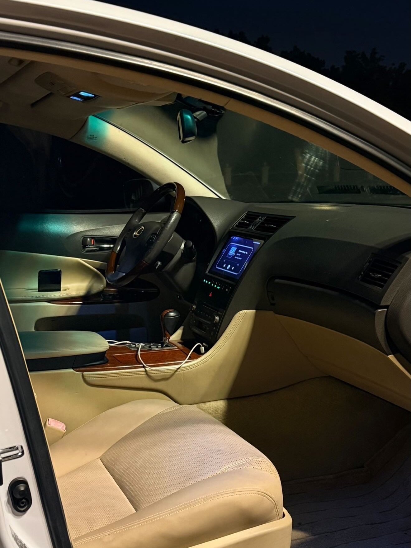 Interior of a car at night. The car appears to be a luxury sedan with a beige leather interior. The dashboard and steering