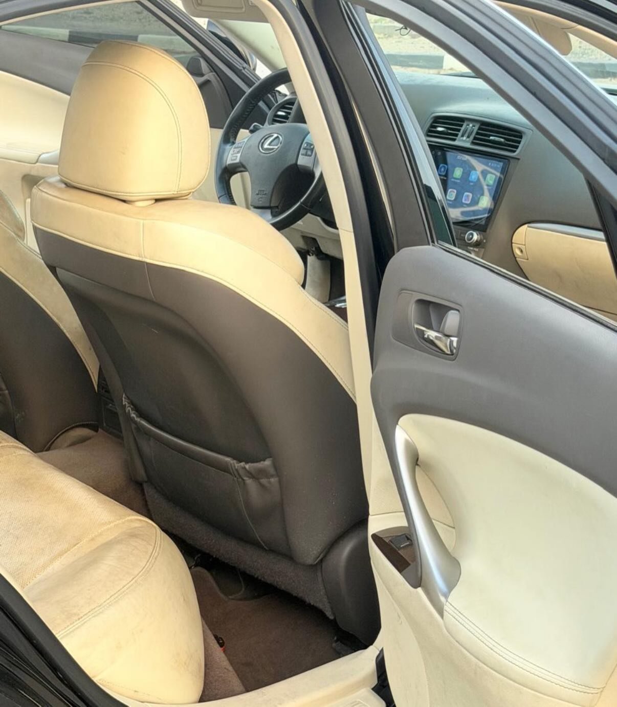 Interior of a car, specifically the driver's seat. The car has beige leather seats and a black steering wheel. The dashboard