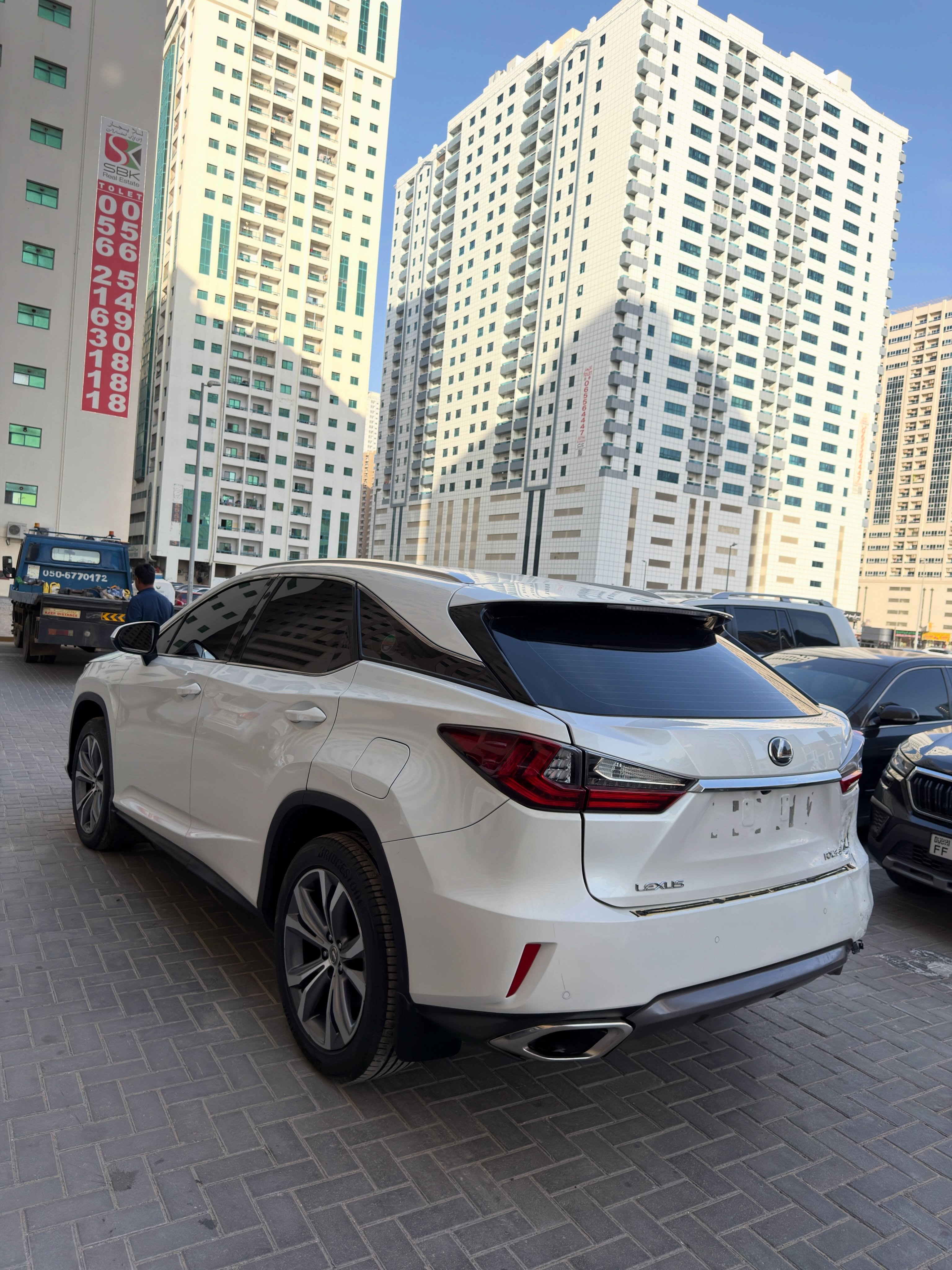 White Lexus SUV parked in a parking lot in front of a tall building. The car is facing towards the right side of the image