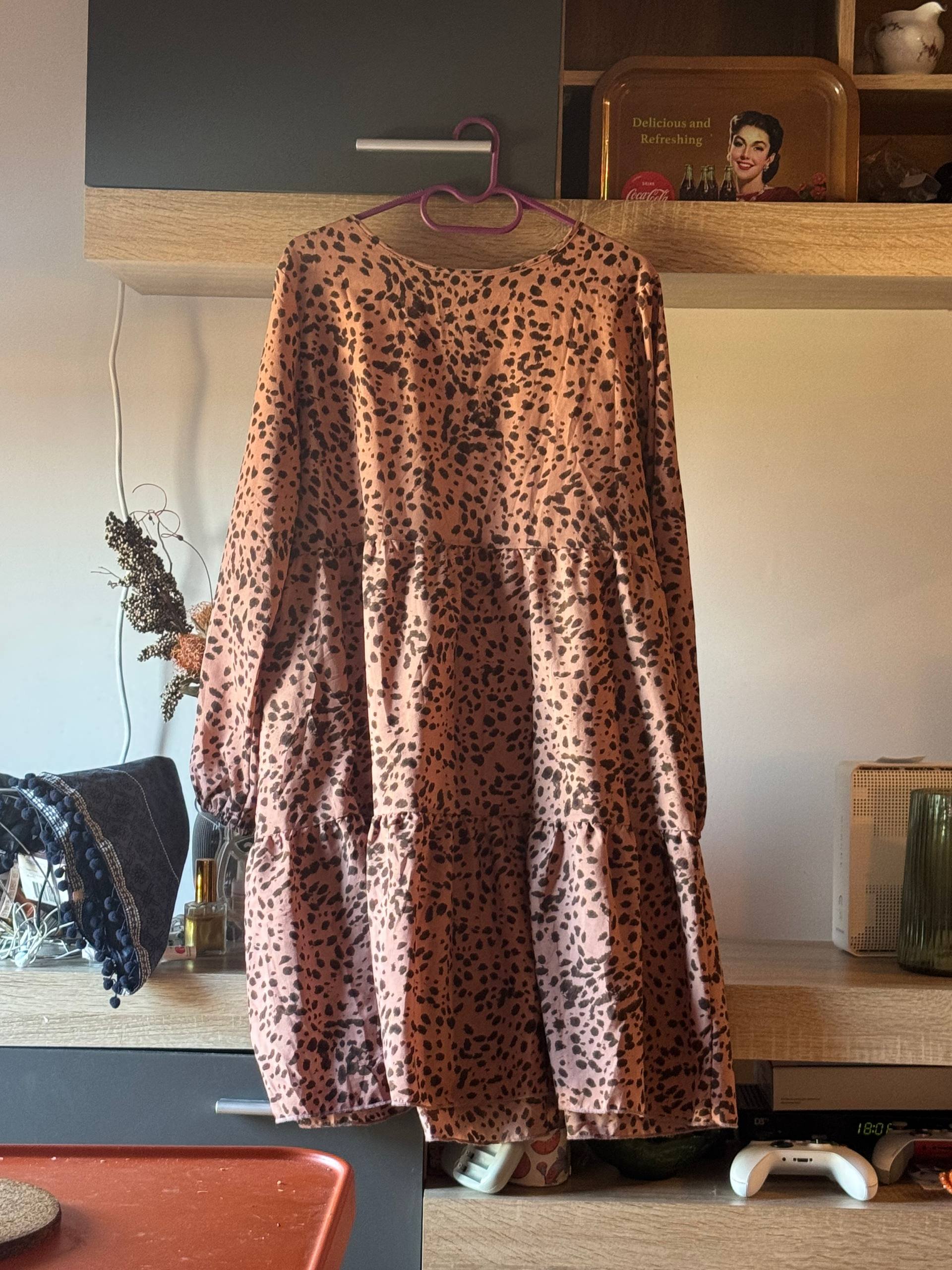 Long dress hanging on a pink hanger in a kitchen. The dress is made of a light pink fabric with a leopard print pattern. It