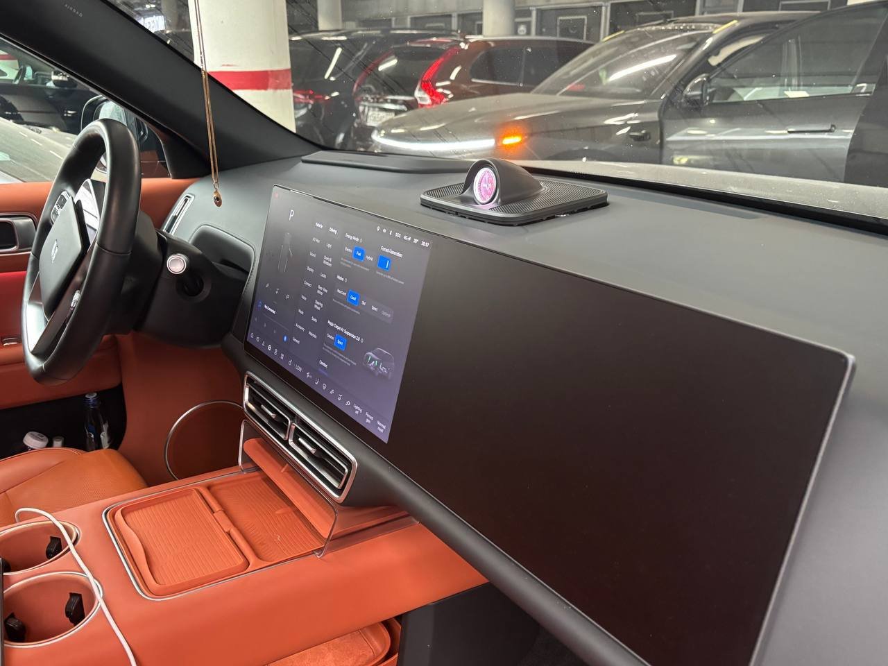 Interior of a car, specifically the driver's seat and dashboard. The dashboard is black and has a large touch screen display