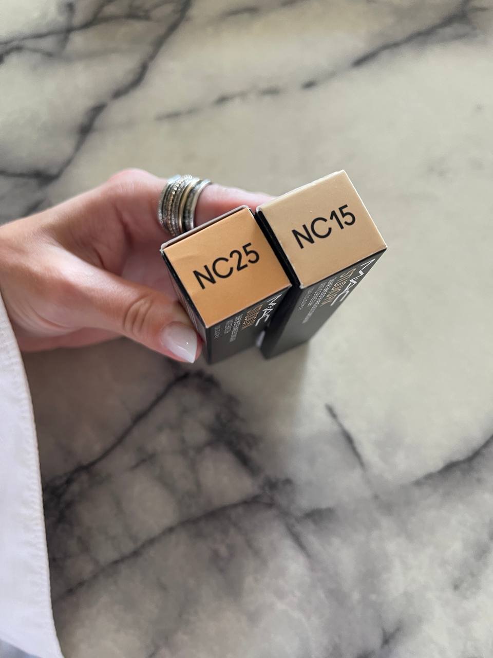 Hand holding two small boxes with the text "NC25" and "NC15" written on them. The boxes are rectangular in shape and appear