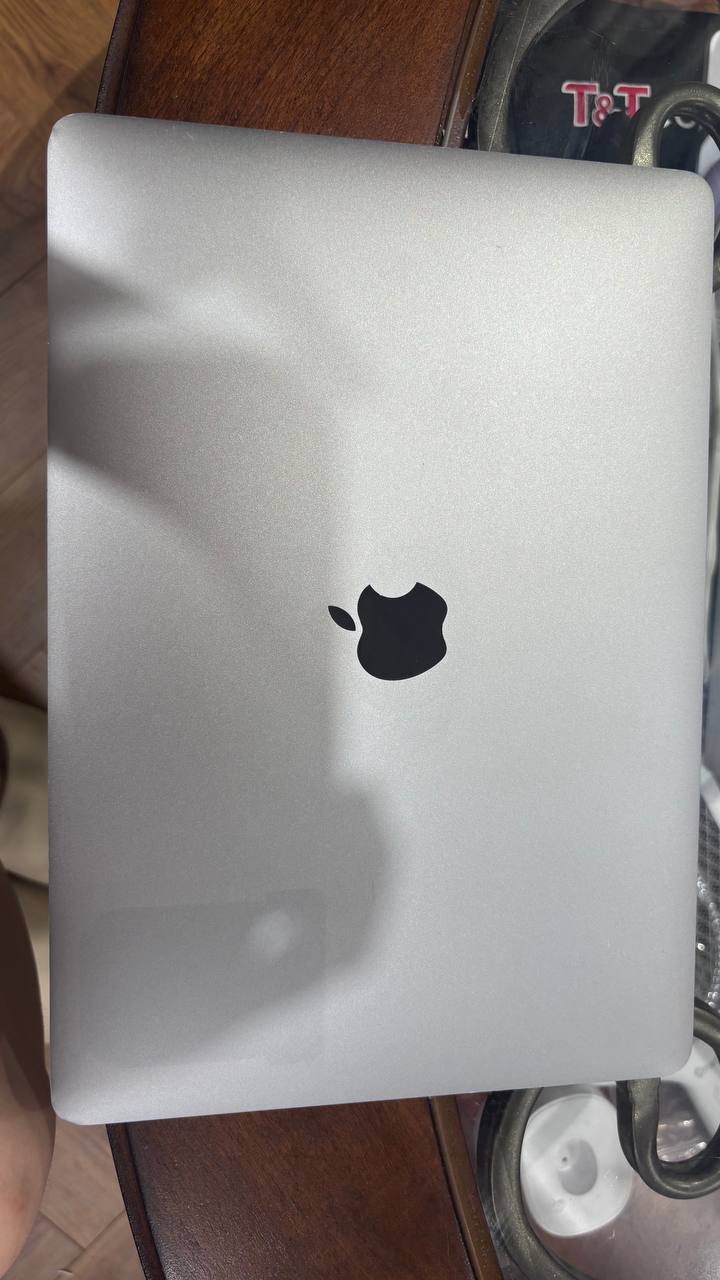 Silver Apple laptop computer sitting on top of a wooden table. The laptop is open and the screen is turned on, revealing the