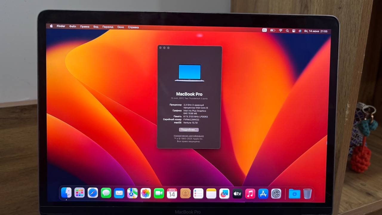 MacBook Pro laptop on a wooden desk. The laptop screen displays the macOS Pro operating system with a red and orange