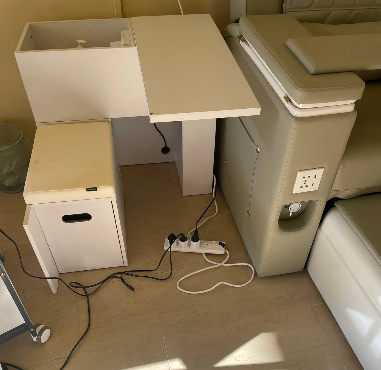 Corner of a room with a beige-colored sofa and a white desk. The desk has a rectangular top with a drawer on the left side