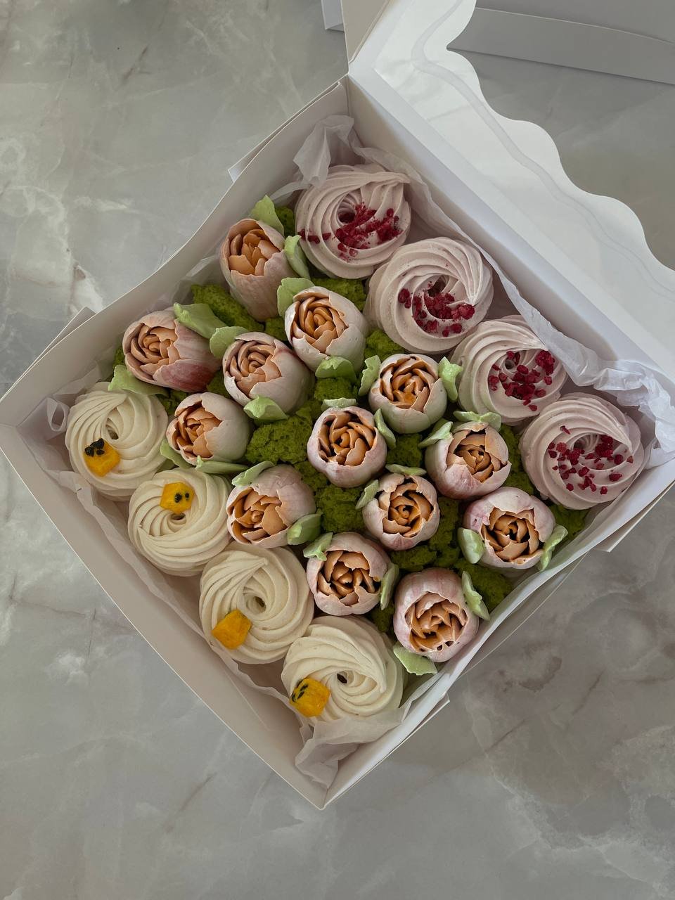 White cardboard box filled with a variety of cupcakes. The cupcakes are arranged in a circular pattern, with each cupcake