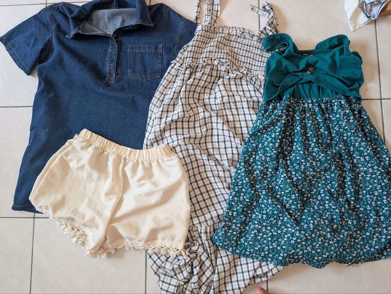 Flat lay of three children's clothing items on a white tiled floor. On the left, there is a blue denim shirt with a