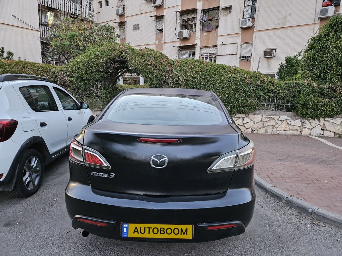 Black Mazda car parked on the side of a street. The car has a license plate that reads "AUTOBOOM". The street is lined with