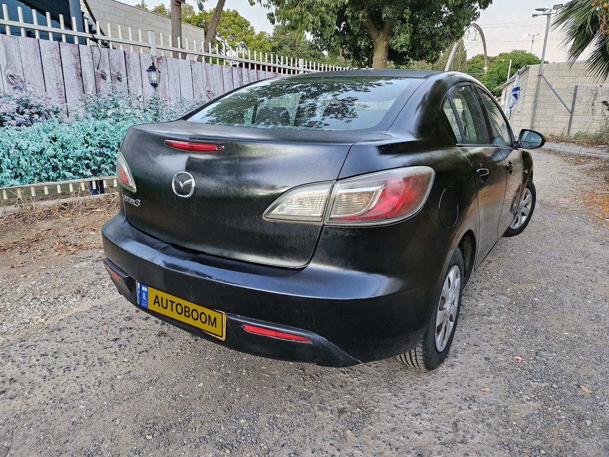 Black Mazda car parked on a gravel road. The car is facing towards the left side of the image and is positioned at an angle.