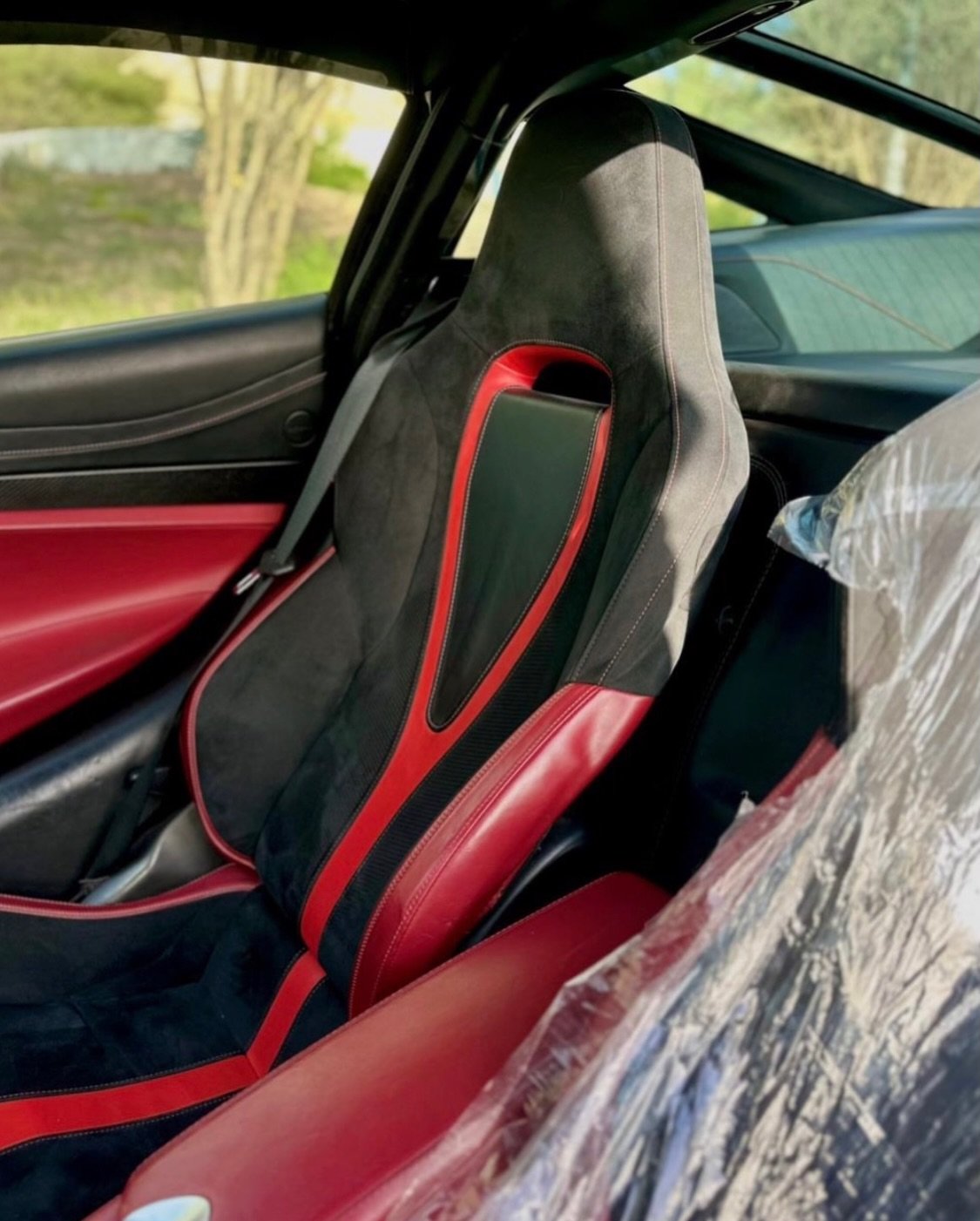 Interior of a car, specifically the driver's seat. The seat is black with red stitching and has a unique design with a
