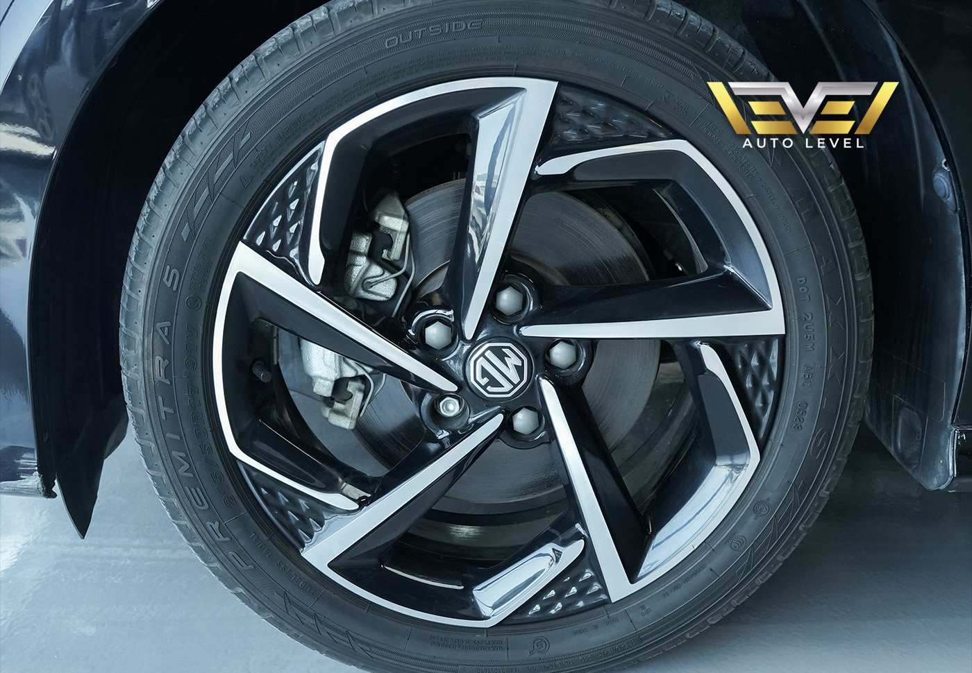 Close-up of a car wheel and tire. The wheel is black with silver accents and has the logo of the car brand "EV1 Auto Level"