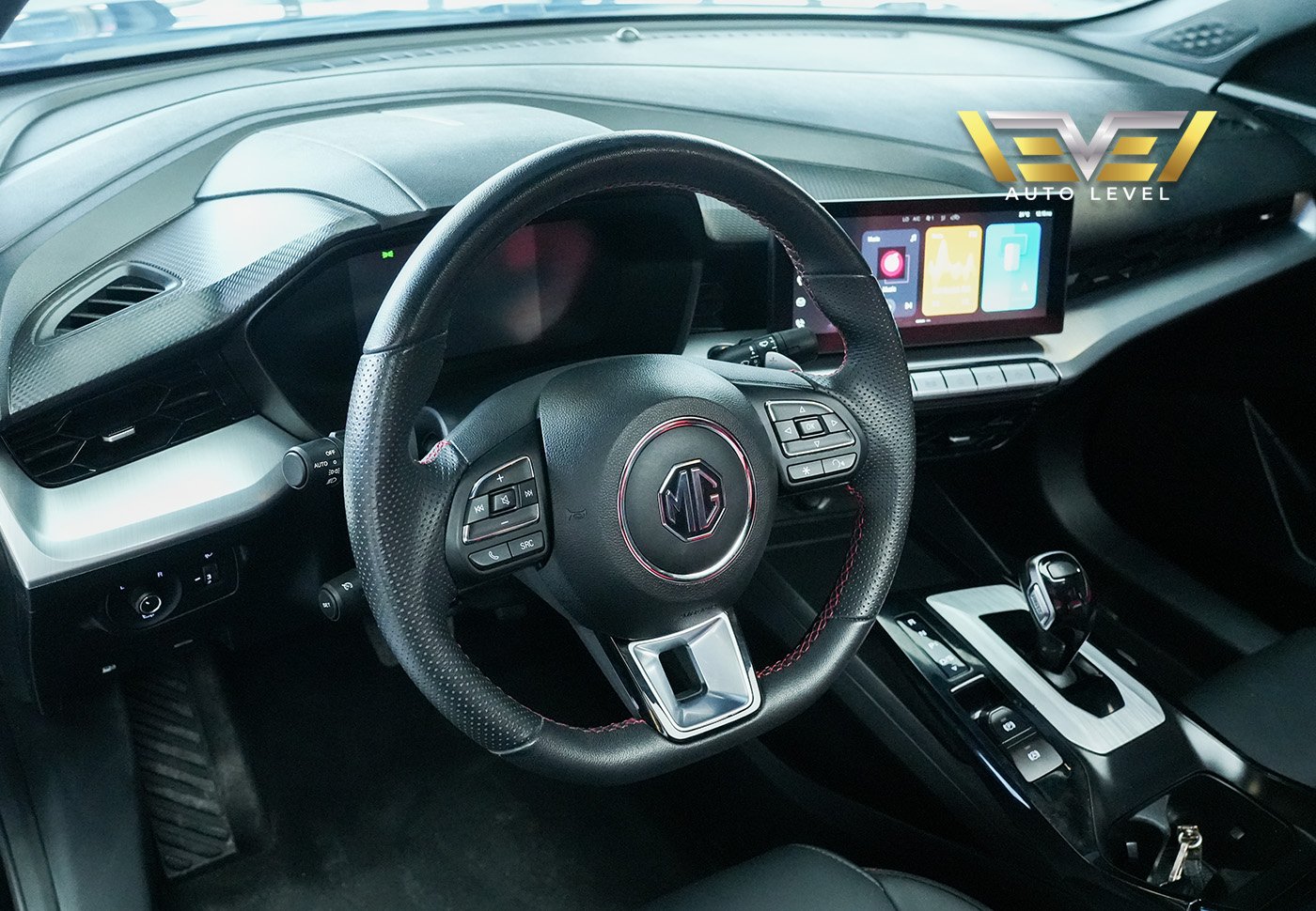 Interior of a car, specifically the driver's seat and dashboard. The steering wheel is black with a red and silver emblem in