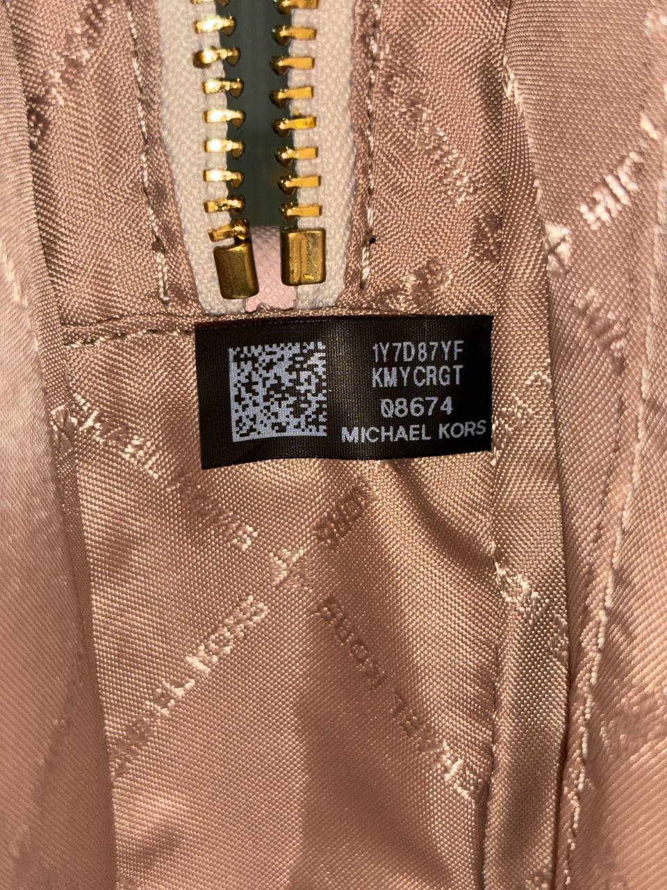 Close-up of a zipper with a label on it. The label is black with white text and a QR code. The text reads "1YTD87YF KMYCRGT