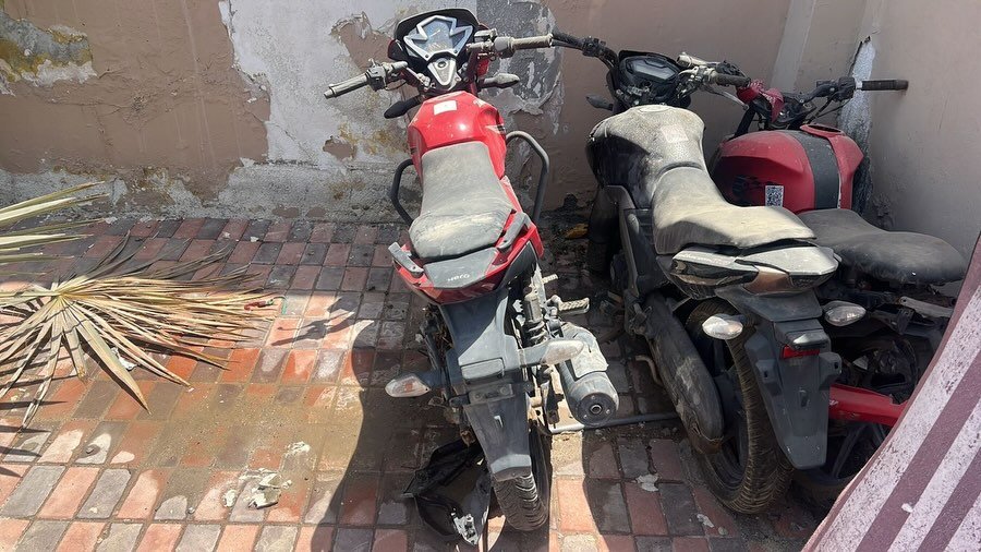 Two motorcycles parked next to each other on a tiled floor. The motorcycle on the left is red and black in color and has a