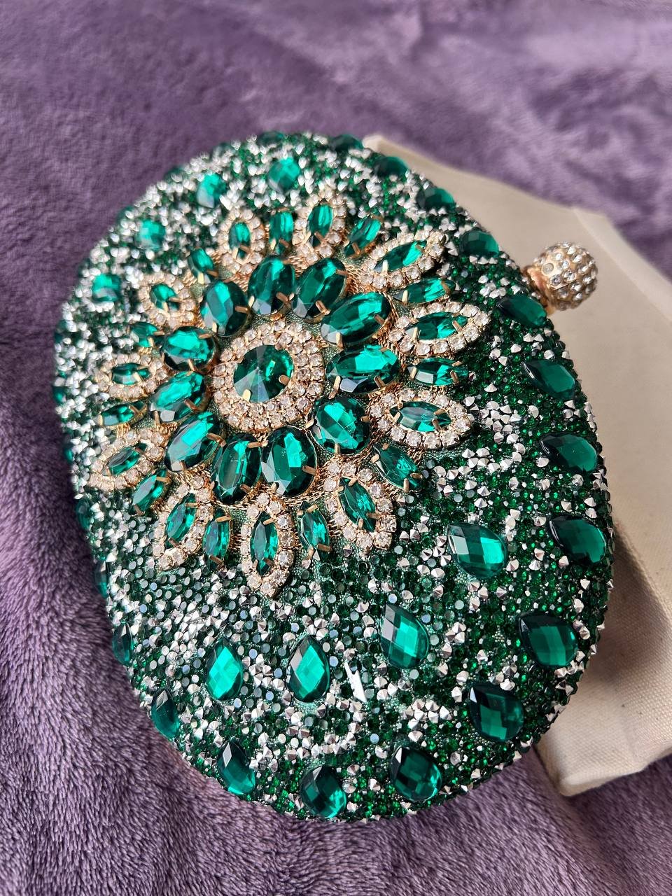 Round, emerald-colored clutch or clutch bag. The bag is made up of multiple rows of small, round, green stones that are