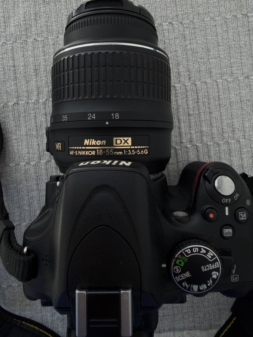 Black camera with a black strap attached to it. The camera is a DSLR with a large lens and a small LCD screen attached to