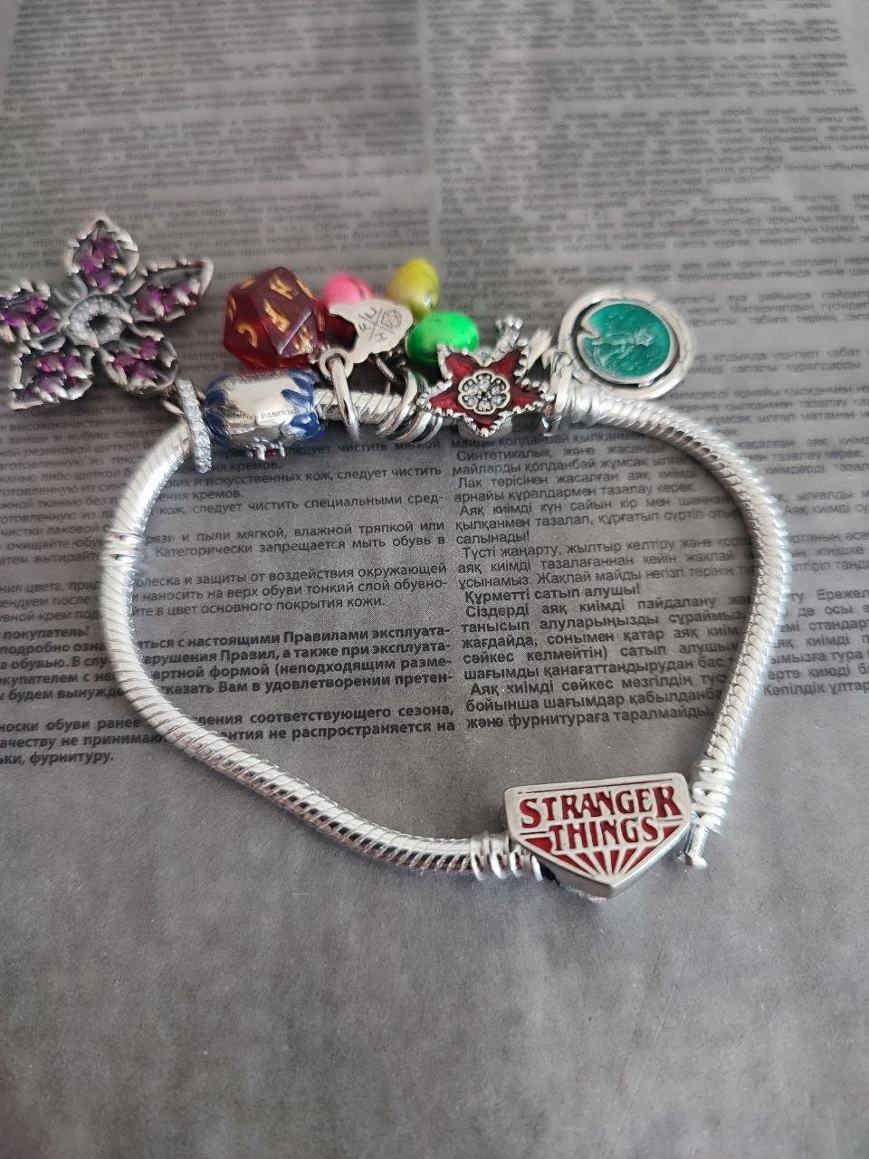 Silver bracelet with various charms and charms attached to it. The bracelet is resting on a piece of paper with the words