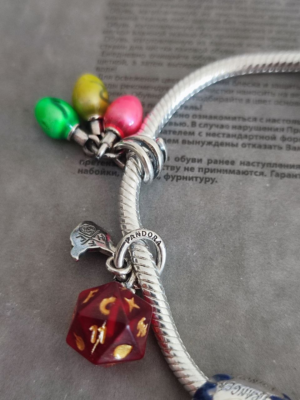 Close-up of a silver bracelet with a charm attached to it. The charm is in the shape of a red dice with gold numbers on it.