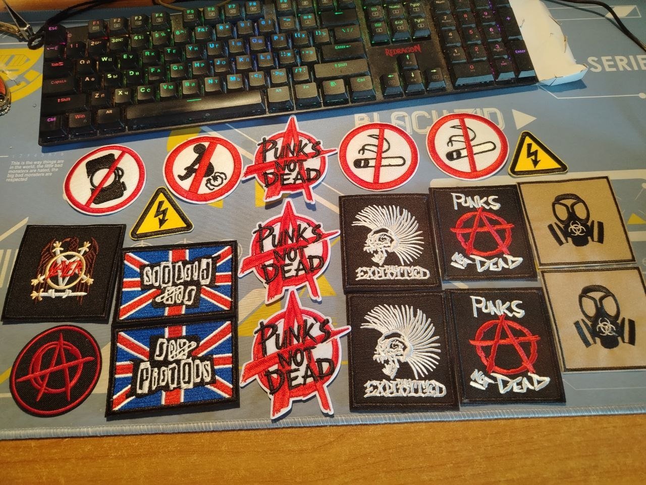 Desk with a keyboard and various patches scattered across it. The patches are of different designs and colors, including