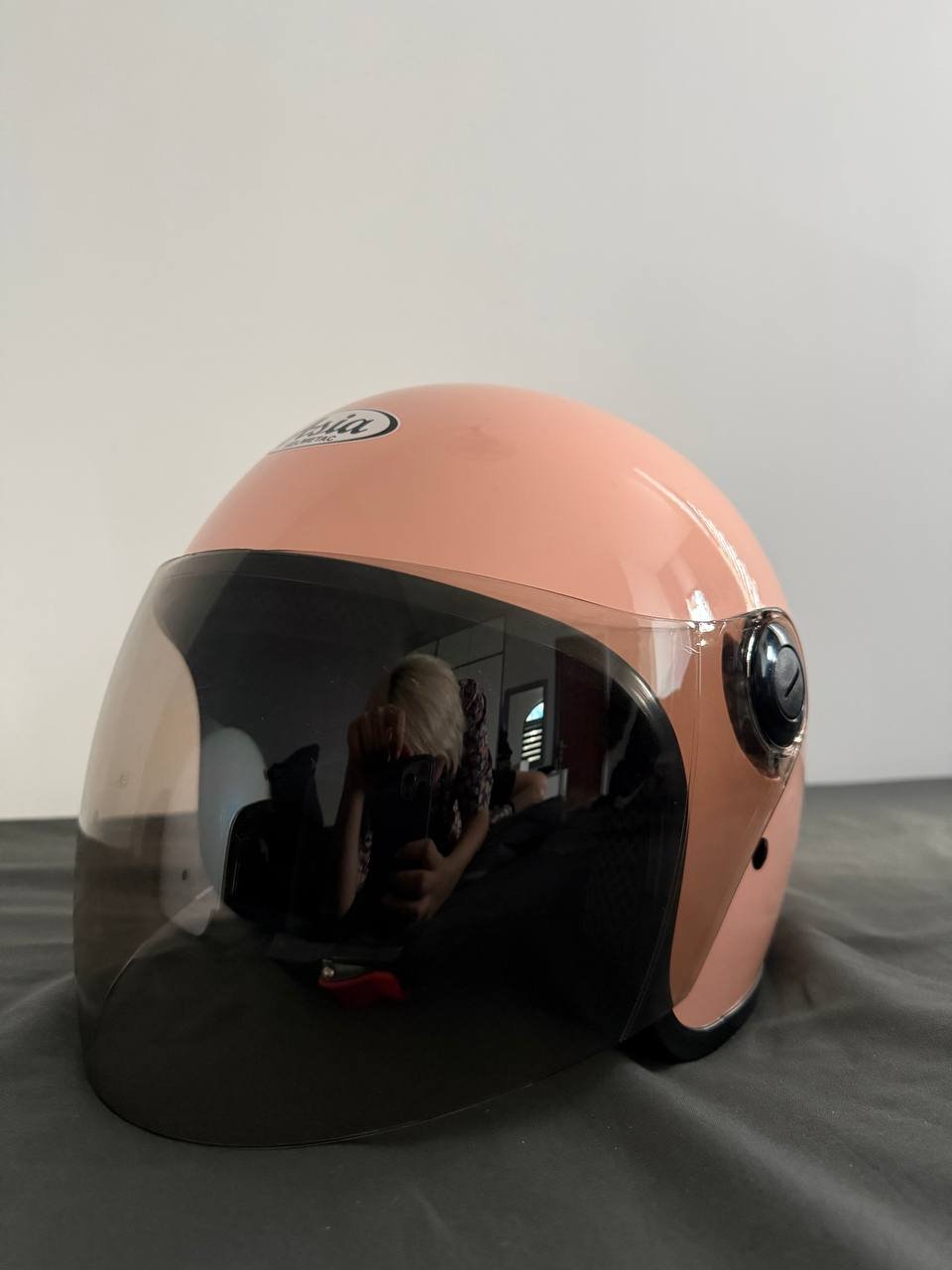 Pink helmet with a clear visor. The helmet is placed on a grey surface and is facing towards the right side of the image.