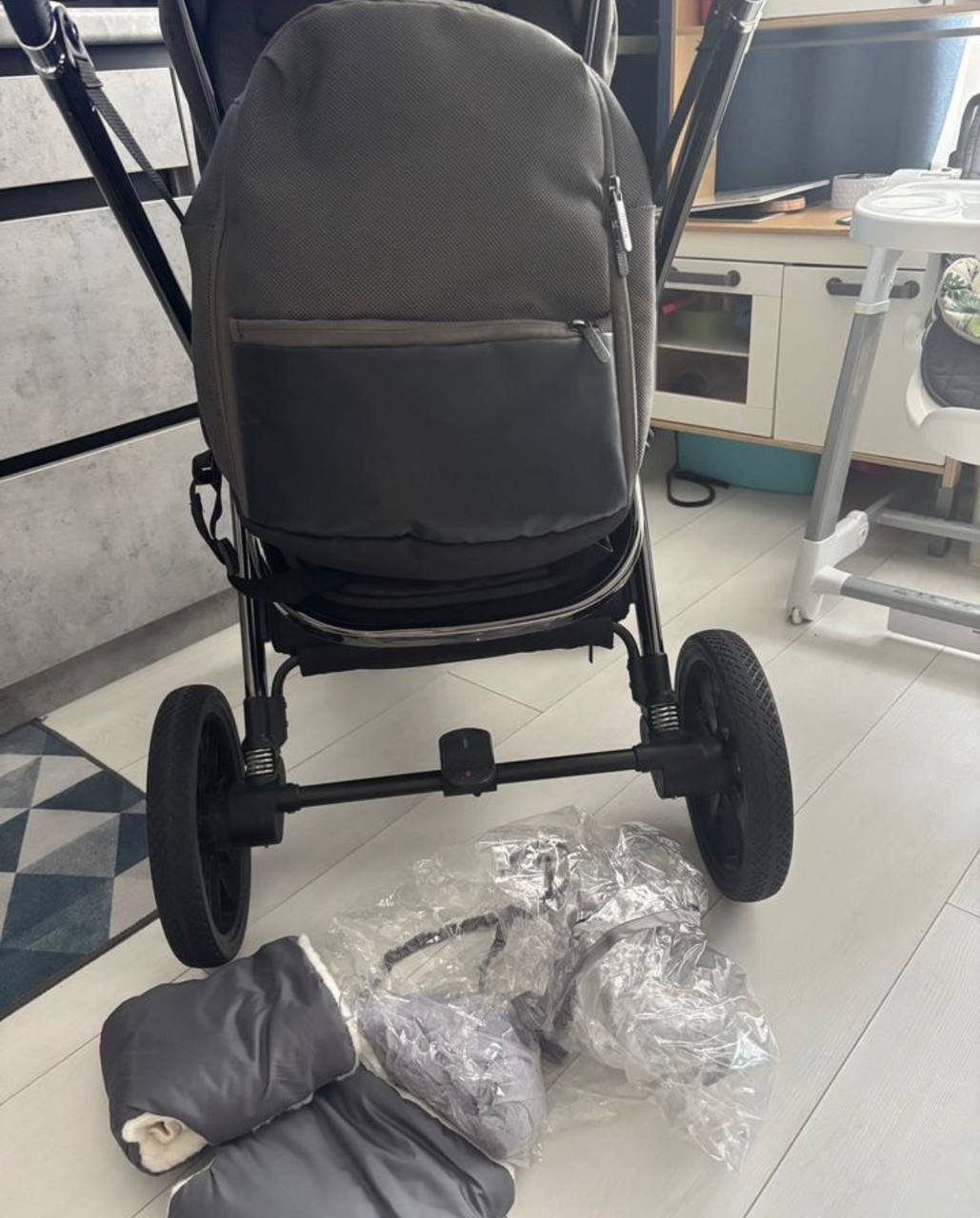 Baby stroller with a grey seat and black frame. The stroller is placed on a white tiled floor in a room with a blue and