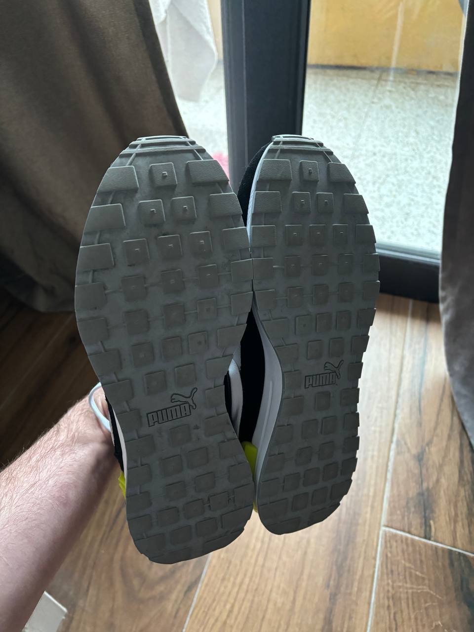 Pair of black Puma sneakers on a person's feet. The soles of the sneakers are black with the Puma logo in white on the heel.