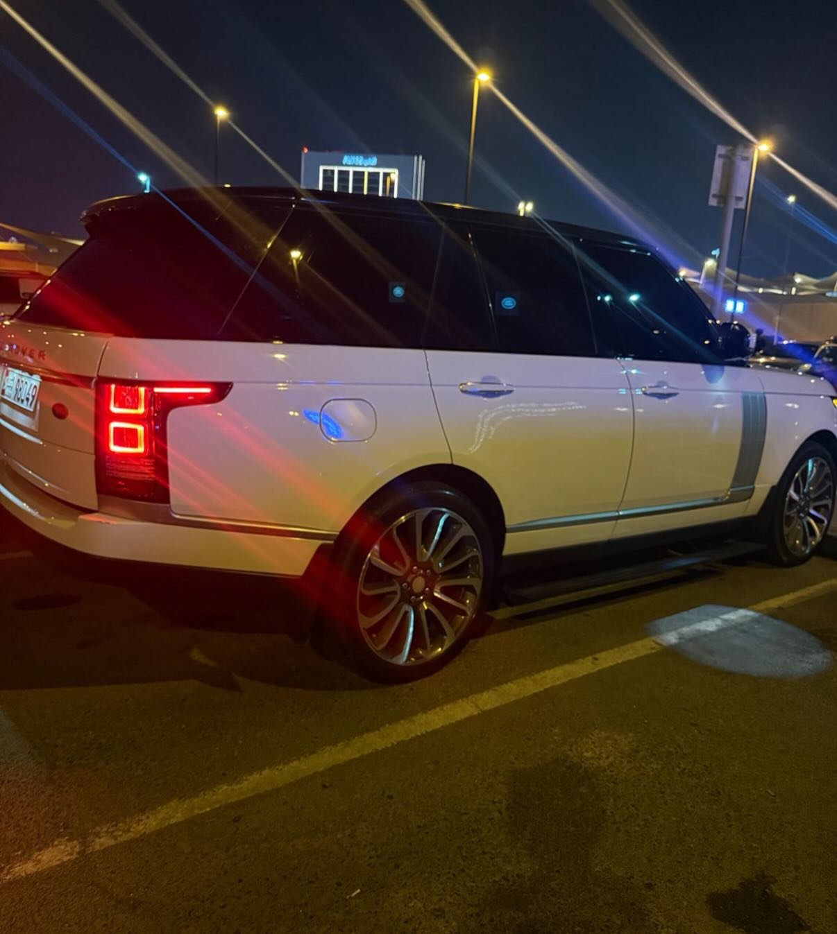 White Range Rover parked in a parking lot at night. The car is facing towards the right side of the image and is positioned
