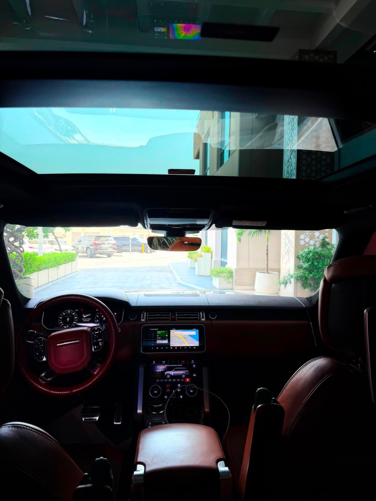 Interior of a car, specifically the driver's seat and dashboard. The car has a large sunroof that covers the entire