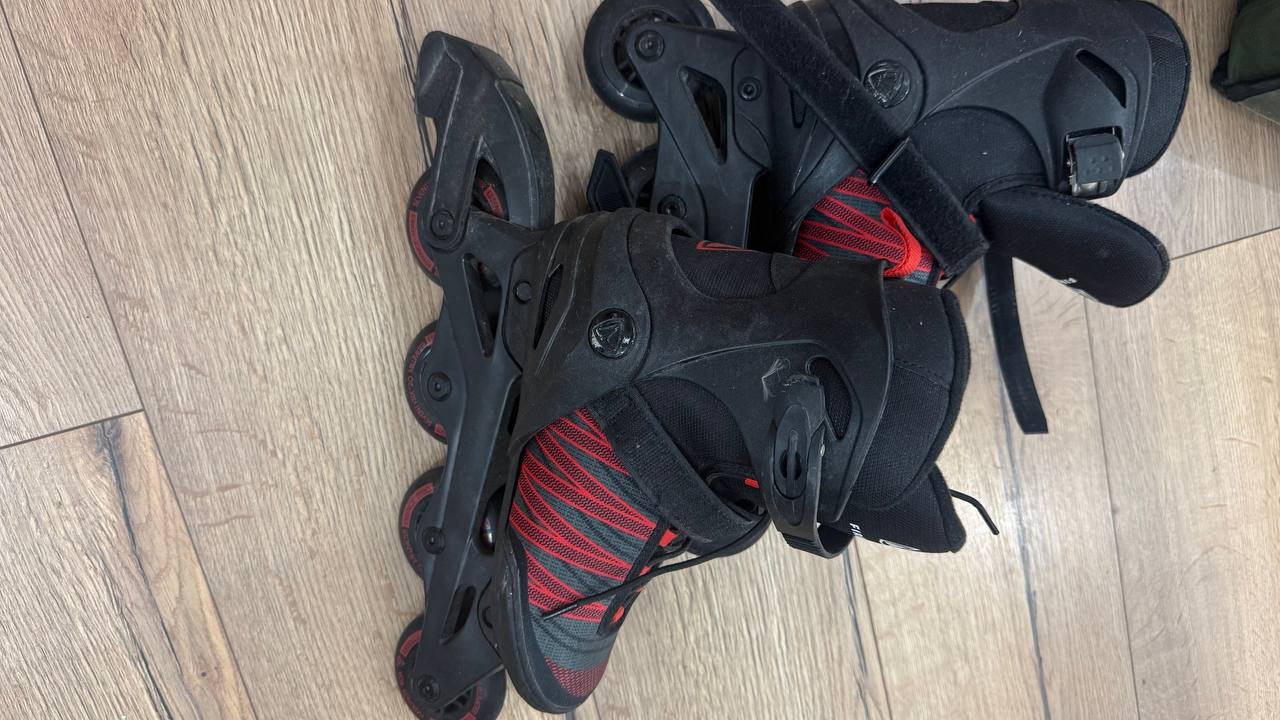 Pair of black roller skates with red and black stripes on them. The skates are placed on a wooden floor, and the straps are