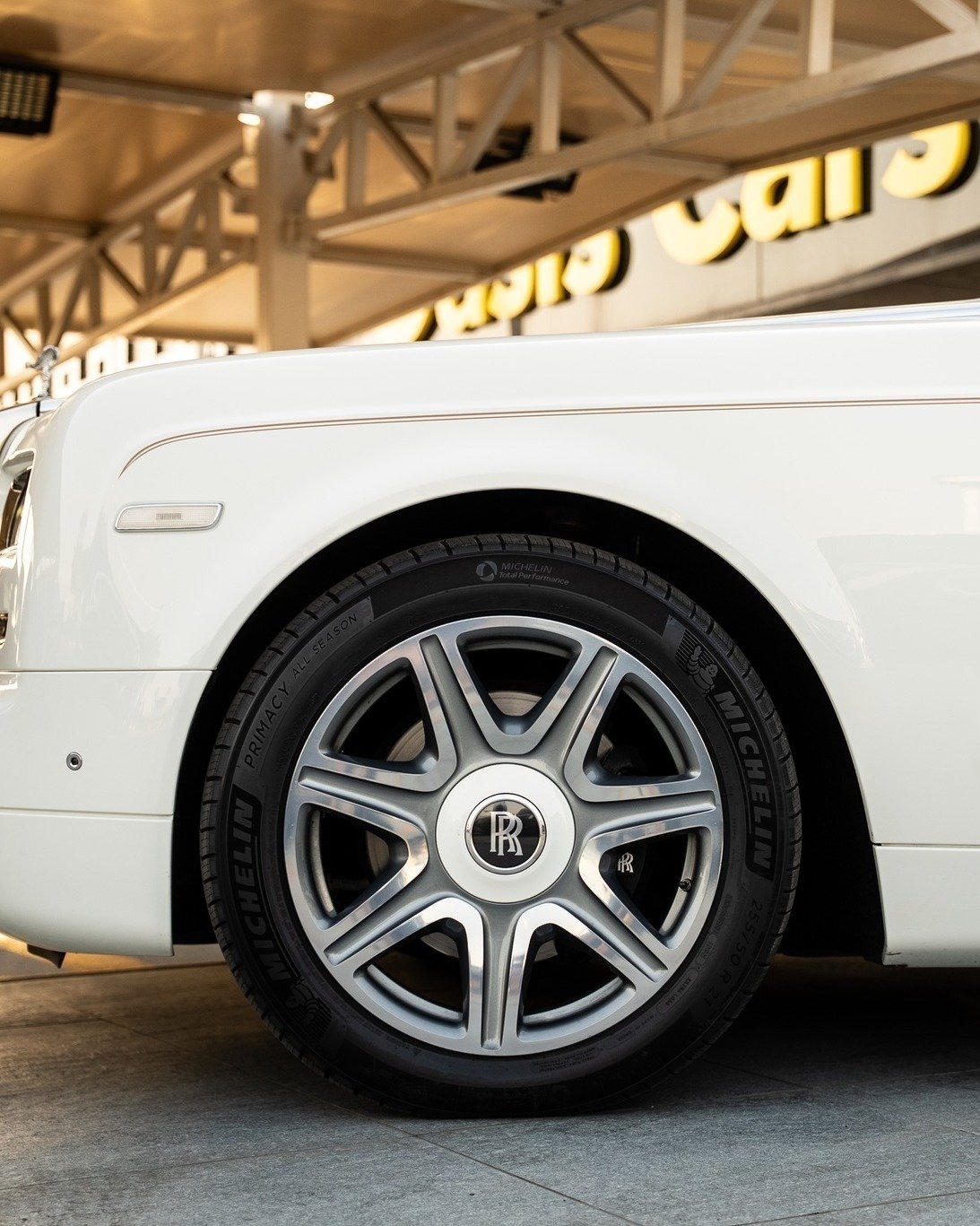 Close-up of the front wheel of a white Rolls-Royce car. The wheel is silver with a black rim and has the iconic Rolls Royce