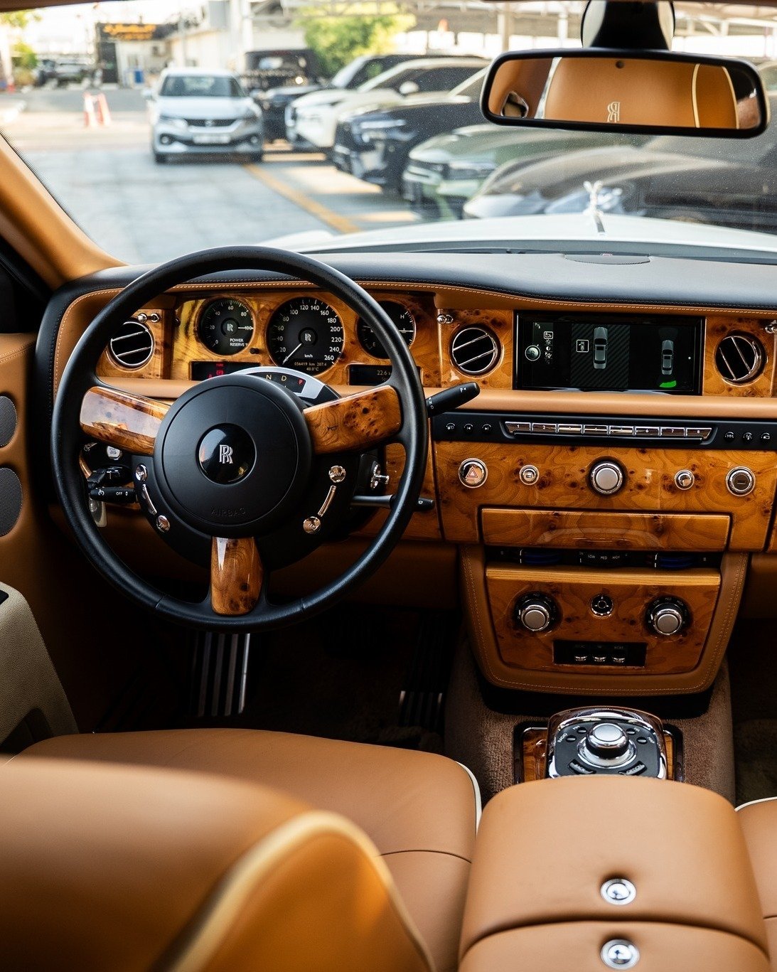 Interior of a luxury car, specifically the driver's seat and dashboard. The car has a wooden panel with various buttons and