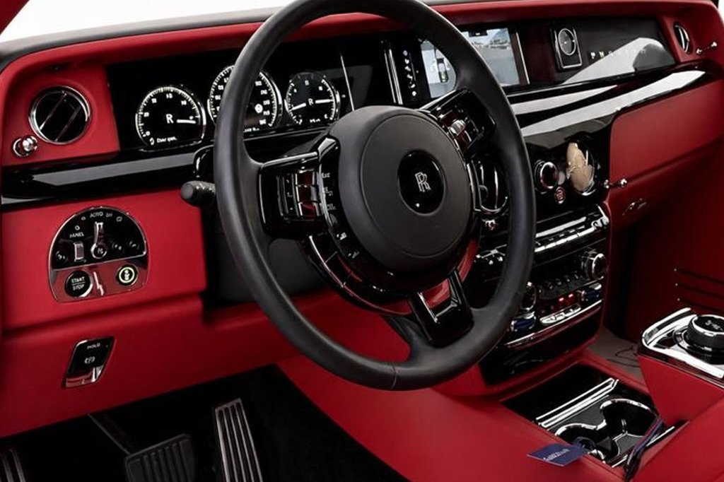 Interior of a luxury car, specifically the driver's seat and dashboard. The car has a black leather steering wheel with the