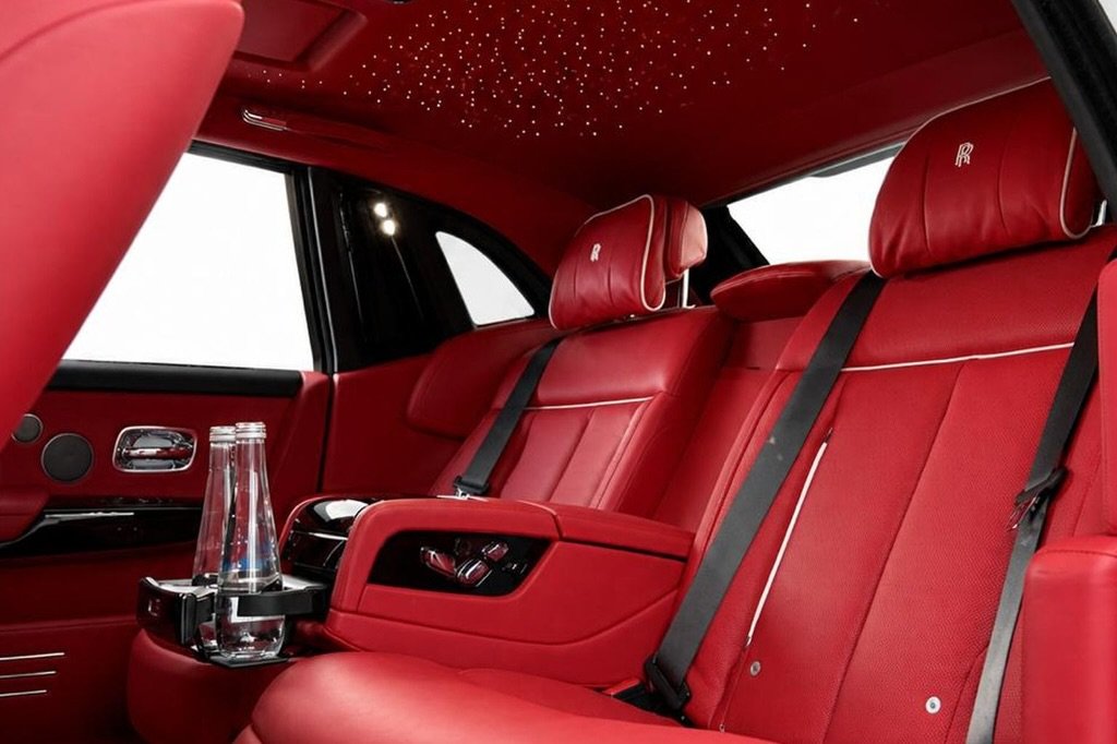 Interior of a luxury car, specifically the back seats. The seats are covered in red leather with the iconic Rolls-Royce logo