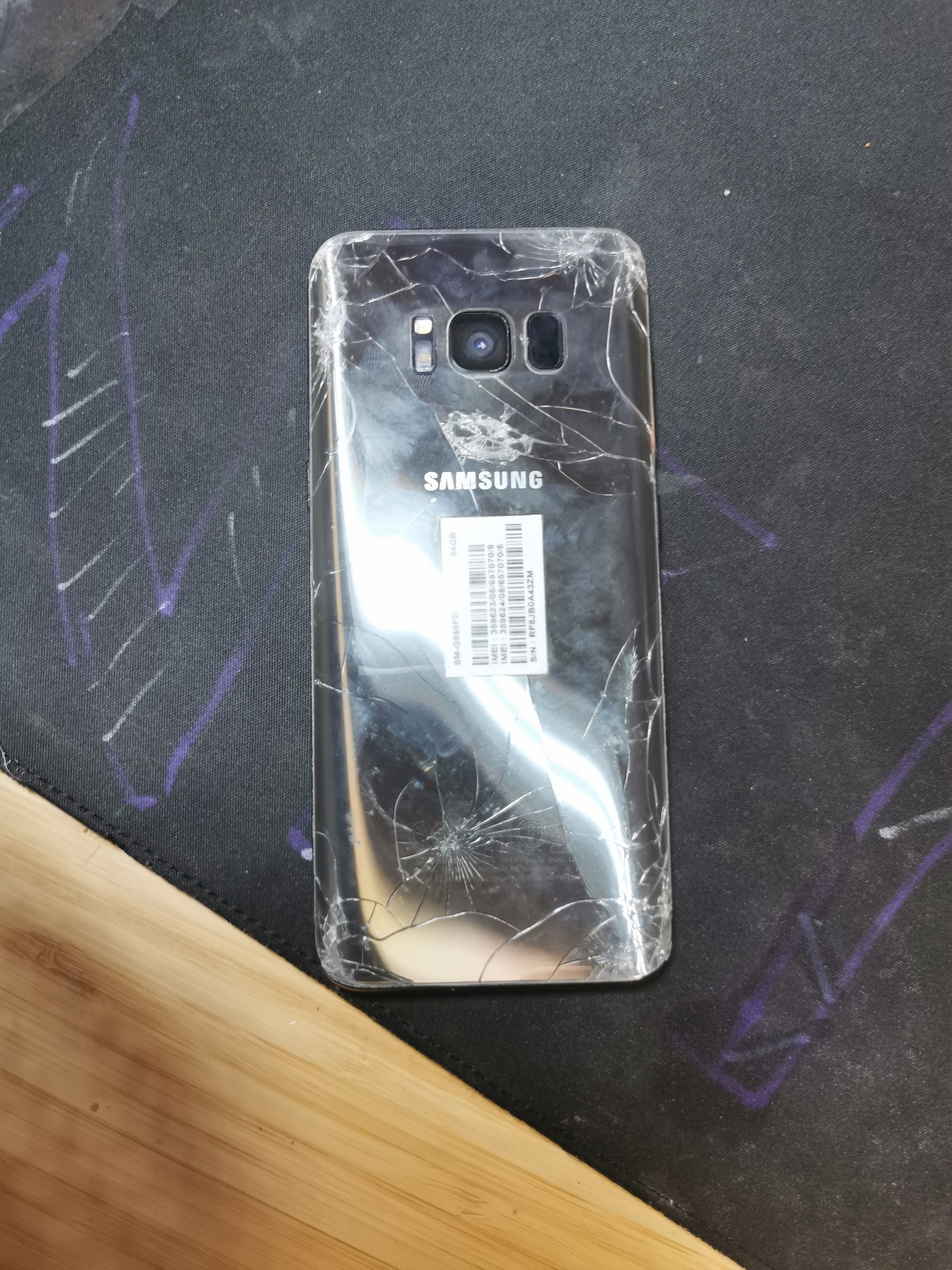 Back of a Samsung smartphone. The phone is lying on a black surface with purple graffiti on it. The back of the phone is
