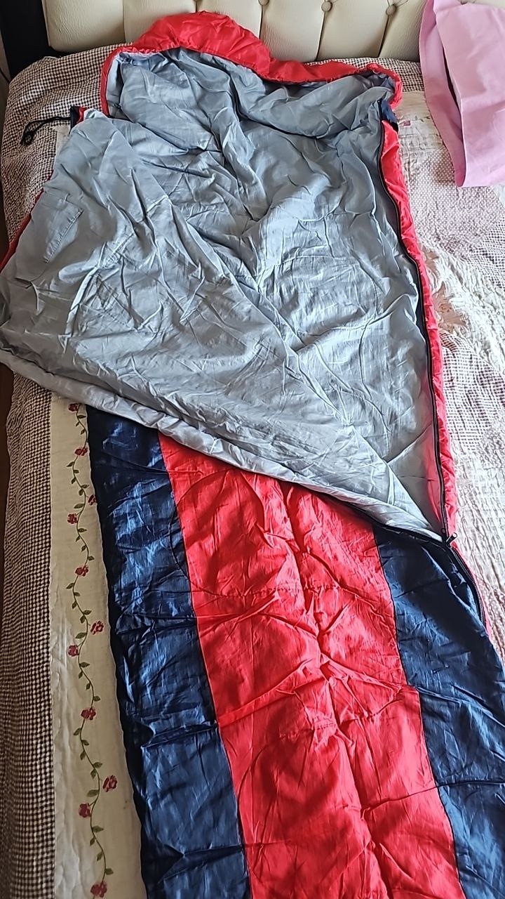 Sleeping bag on a bed. The sleeping bag is made of a red and blue quilted material and is folded neatly on top of a white