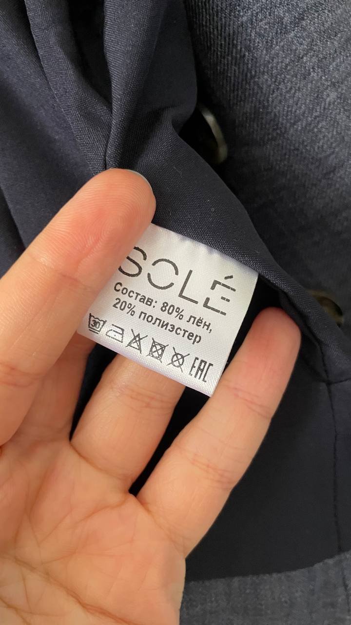 Close-up of a person's hand holding a label that reads "SOLÉ" in Russian. The label is rectangular in shape and has a white