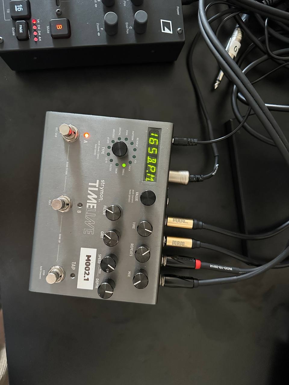 Black electronic device with multiple knobs and buttons on its front panel. The device appears to be a mixer or a control