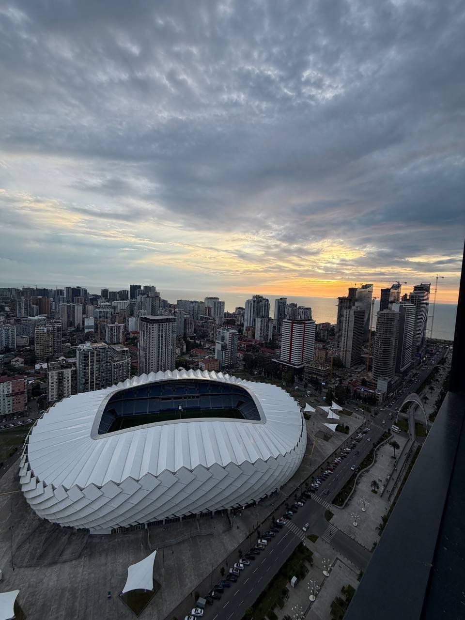 Aerial view of a city skyline at sunset. The sky is filled with dark, ominous clouds and the sun is setting in the