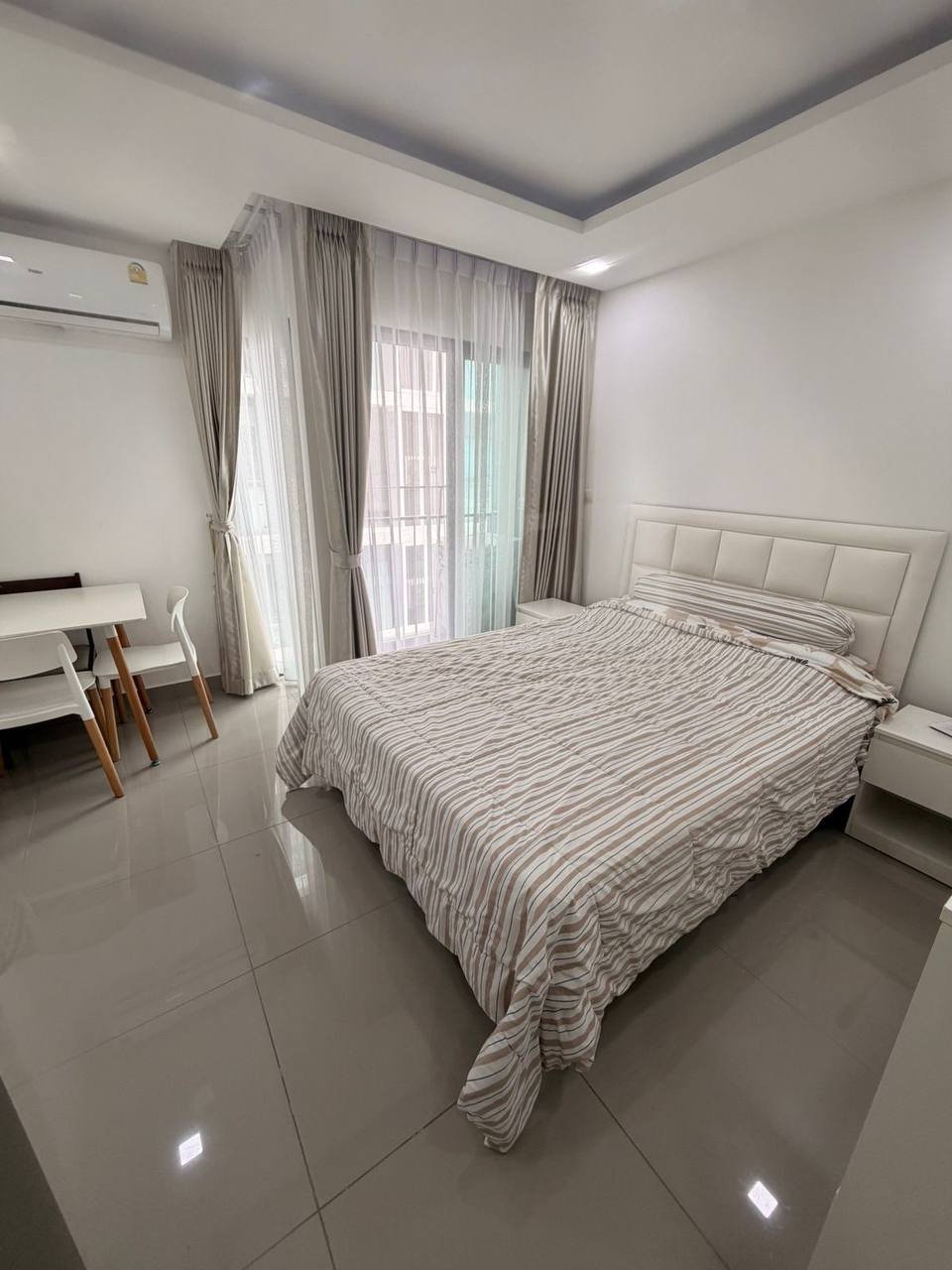 Modern and minimalist bedroom with a large bed in the center. The bed has a white headboard and a striped comforter with red