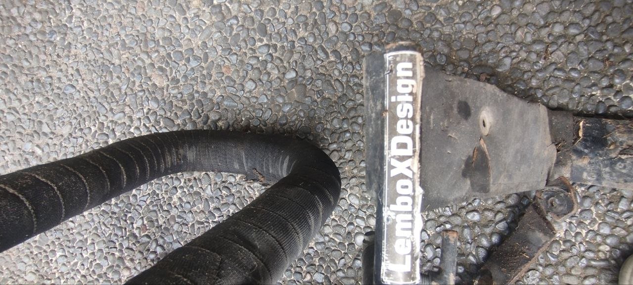 Close-up of a black hose lying on a gravel ground. The hose appears to be made of rubber or a similar material and is coiled