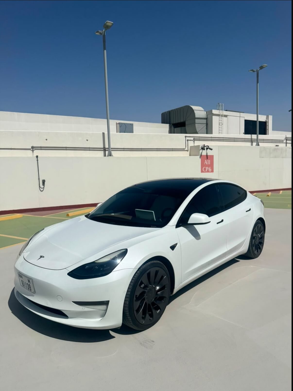 White Tesla Model 3 car parked in an empty parking lot. The car is facing towards the left side of the image and is