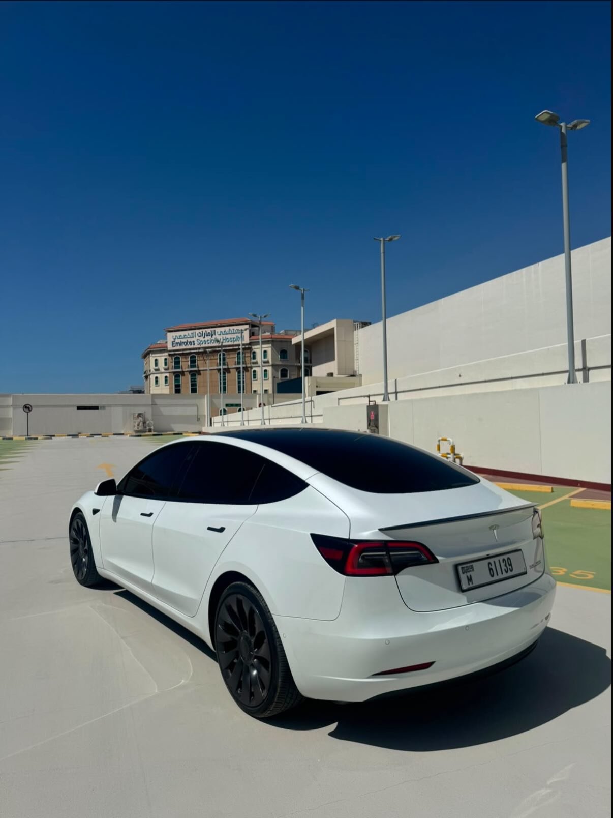 White Tesla Model S car parked in an empty parking lot. The car is facing towards the right side of the image and is