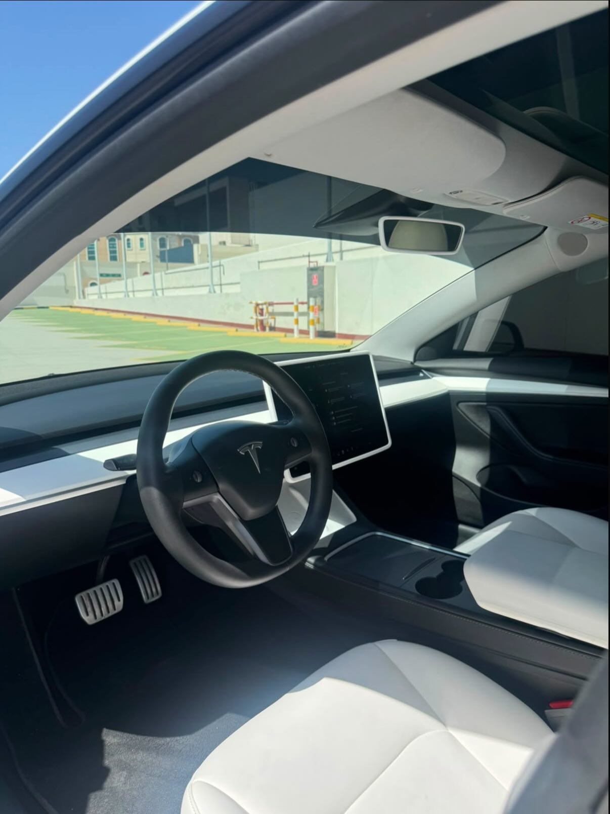 Interior of a Tesla Model S car. The car has a black steering wheel with the Tesla logo in the center. The dashboard is