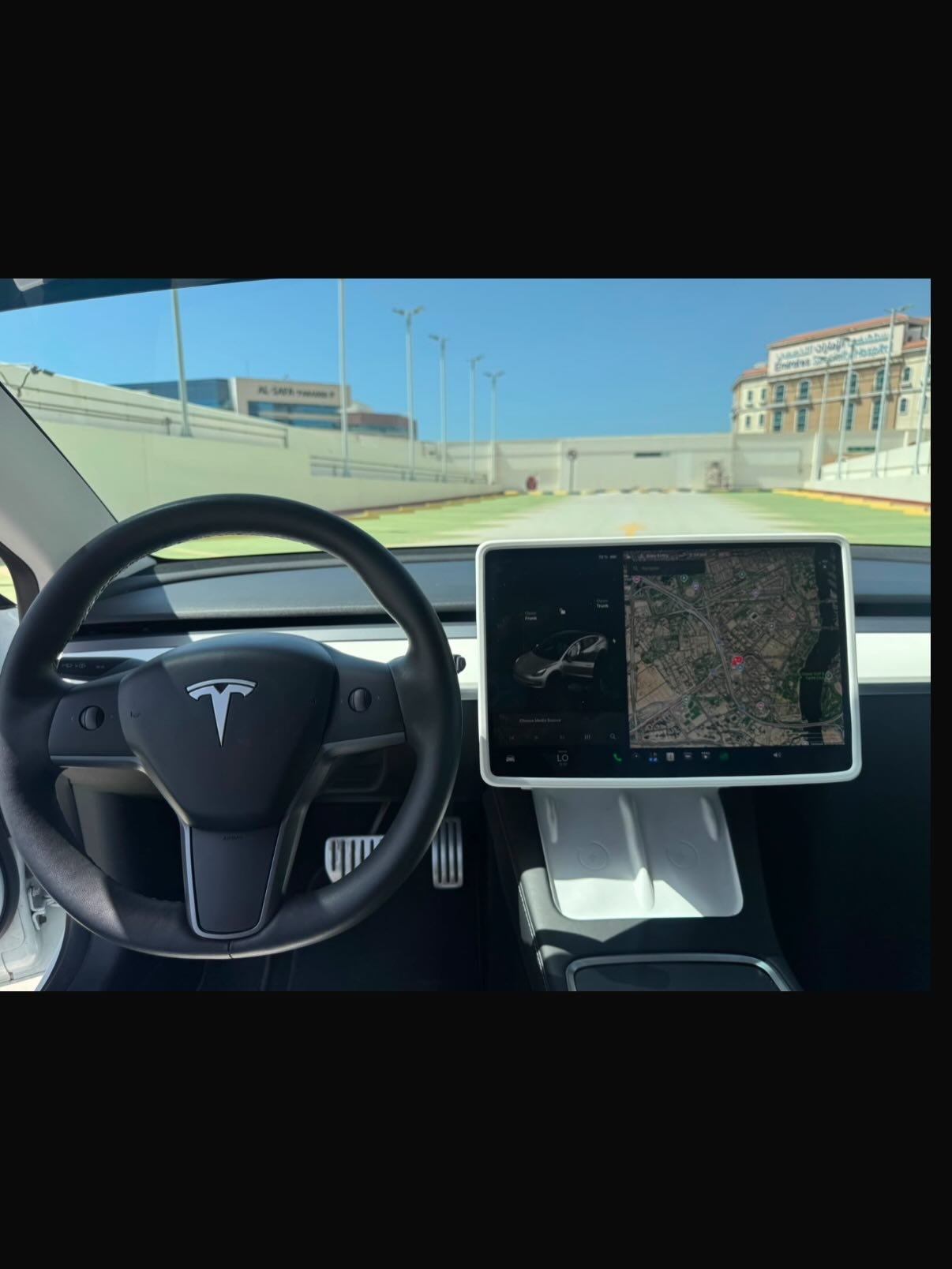 Interior of a Tesla car, with the steering wheel and dashboard visible. The steering wheel has the Tesla logo in the center