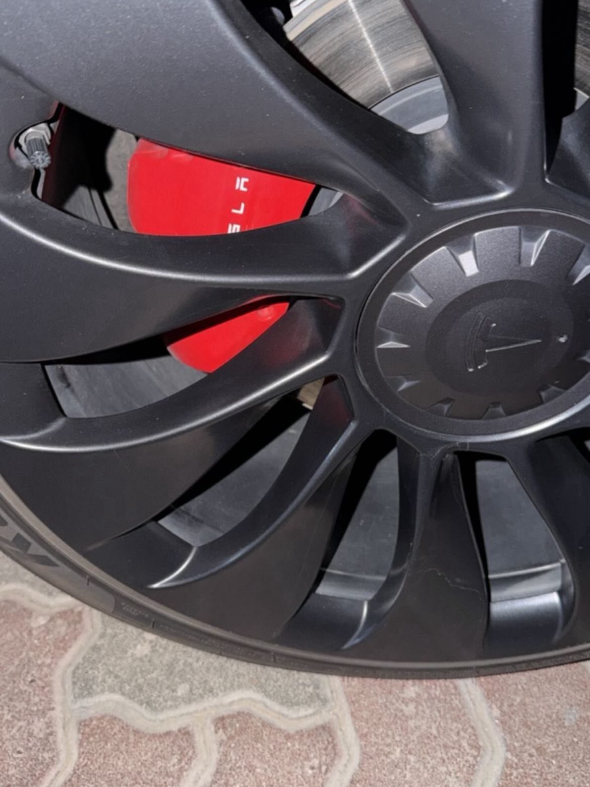 Close-up of a car wheel. The wheel is black with a silver rim and has a red brake caliper in the center. The caliper has a
