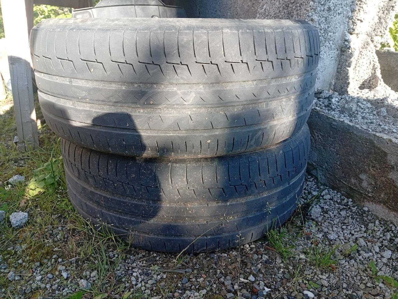 Stack of three black tires stacked on top of each other on a gravel ground. The tires appear to be new and unused, with no
