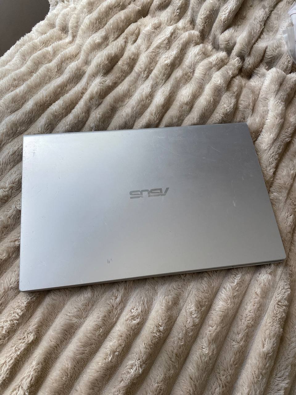 Silver laptop lying on a beige-colored blanket. The laptop is open and the screen is facing towards the right side of the