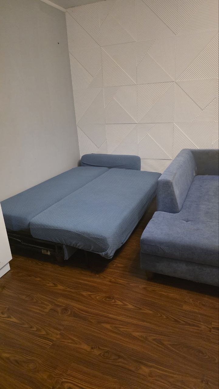 Corner of a room with a wooden floor and a white wall with a geometric pattern. On the left side of the image, there is a