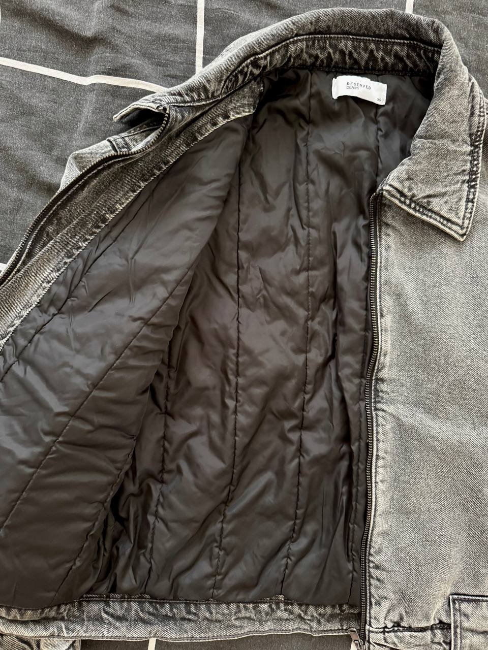 Inside of a gray jacket. The jacket has a quilted design on the left side and a collar on the right side. The collar has a